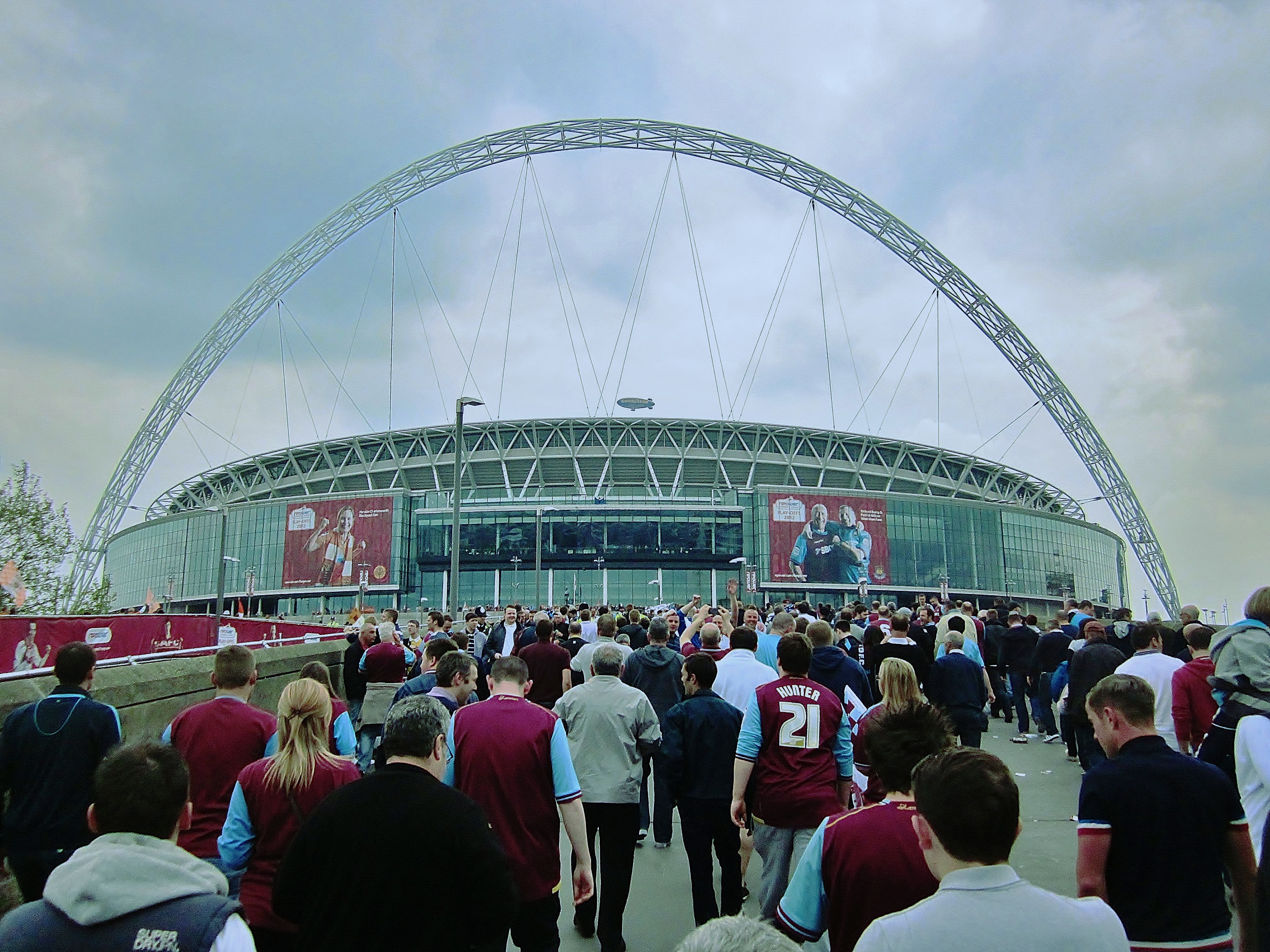 Wembley Stadium with a packed crowd walking towards, dressed in football kits