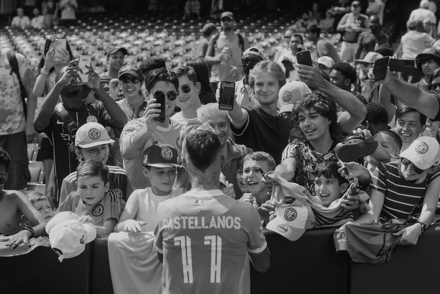 Football player Castellanos faces a crowd of fans with his back turned to the camera and signs autographs